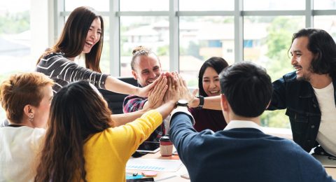 group of young multiethnic diverse people gesture hand high five, laughing and smiling together in brainstorm meeting at office. Casual business with startup teamwork community celebration concept.