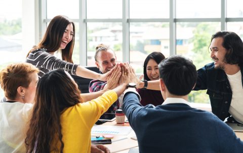 group of young multiethnic diverse people gesture hand high five, laughing and smiling together in brainstorm meeting at office. Casual business with startup teamwork community celebration concept.